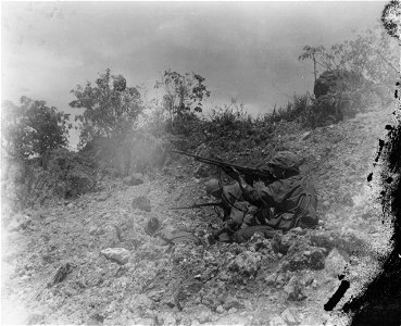 A Marine automatic rifleman fires his weapon 3-400 yards beyond our frontline to protect some wounded Marines in the same hole with him, who are being fired upon by the Japs. Saipan. June, 1944.