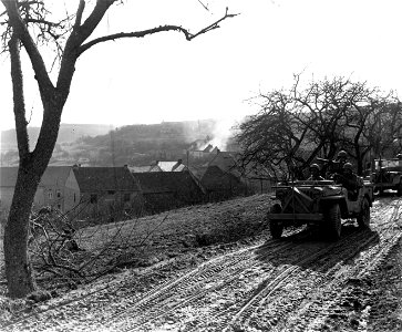 SC 335566 - While the town of Portz, Germany, burns in the background, 10th Armored Division jeeps of the 3rd Army advance on Saarburg, Germany. 21 February, 1945.