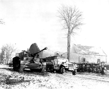 SC 199106 - A knocked-out Nazi tank stands near wrecked houses in Belgian town of Foy, near Bastogne, as 6th Armored Div., 320t Inf. Regt., 26th Div. halftrack passes. January, 1945.