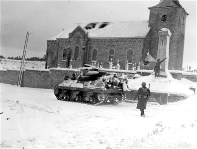 SC 329981 - Tank destroyer moves with infantrymen through town of Bovigny, Belgium. Column in foreground is World War I memorial. 20 January, 1945.