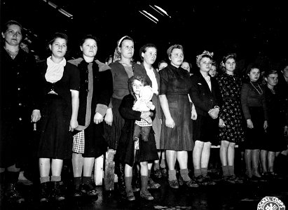 SC 404993 - A small girl with her dolls stands with Russian women members of a Displaced Person's Camp in France, as the United States Band, which entertained them at their camp, plays for them their new Russian national anthem...
