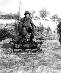 SC 198847 - Pfc. Joseph Locke, Van Nuys, Calif., packs his bedroll and equipment on a small sled for transportation to an advance position in Henimont(?), Belgium.