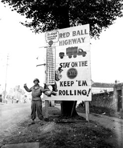SC 195512 - Cpl. Charles N. Johnson, Paris, Tenn., waves on a motor convoy rushing priority materiel to the forward areas in France. 5 September, 1944.