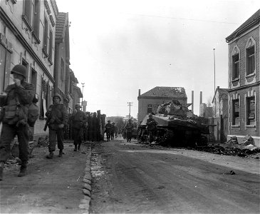 SC 335593 - Infantrymen of 1st U.S. Army march past still-smouldering tank and roadblock in Beuel, Germany. 20 March, 1945.