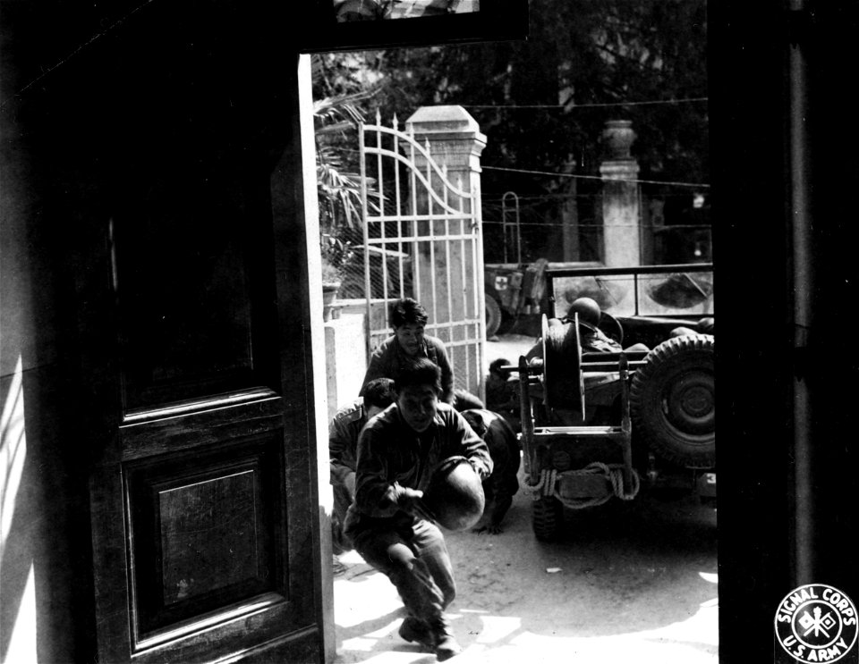 SC 337154 - These infantrymen, Americans of Japanese descent, of the 442nd Regt., run for cover as a German arty. shell is about to land outside the building. 4 April, 1945.