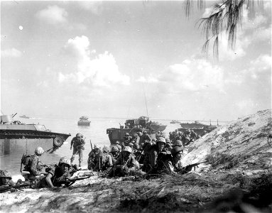 Marines of the first wave, landing on the beach at Saipan, crawl forward for protective covering while waiting for additional waves of green-garbed Leathernecks to land.