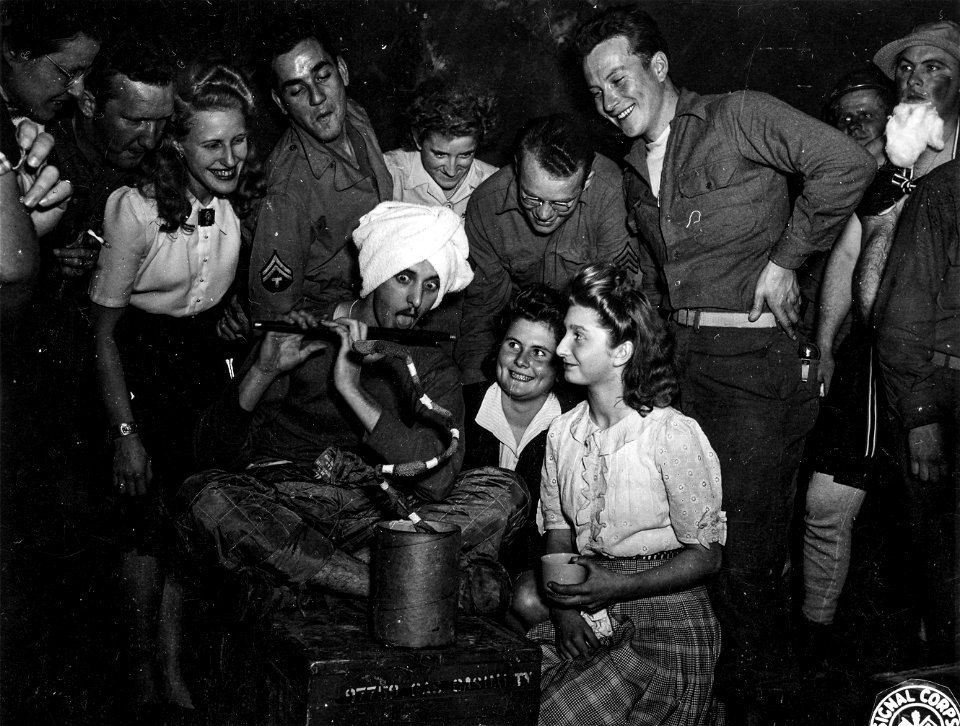 SC 196068 - Complete to a flute, turban, and ersatz snake, TeC 5 Hernry Vin Roten, seated, of Brooklyn, N.Y., muses fellow GIs and pretty guests from the nearby French town of Toul...