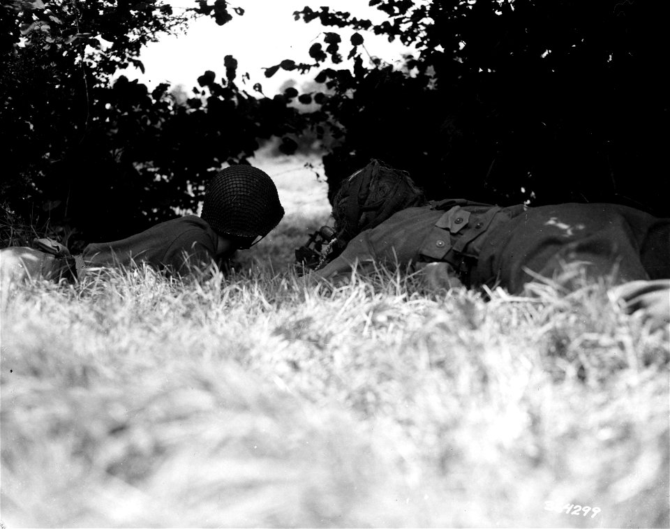 SC 364299 - Two GIs of the 2nd Infantry Division operate a .30 caliber light machine gun from under the cover of low-hanging trees. They are firing at a hedgerow across a clearing. Near Vire, France. 22 August, 1944.