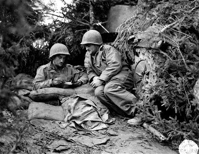 SC 195744 - Soldier in dugout near Aachen, Germany, writes out message on blank while companion waits to deliver it.