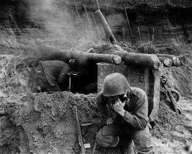 SC 364328 - Mortar fires on enemy positions in the German-held third of Forbach. Officer checks range with observation post over phone as squadman ducks the blast of another round on the way. photo