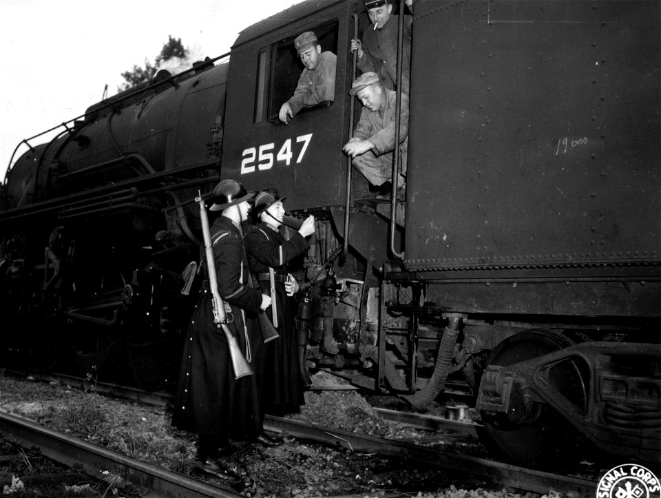 SC 396765 - GI railway men share their cigarettes with two of the Belgian gendarmes who guard the GI supply trains in the railroad yards at Liege, Belgium.