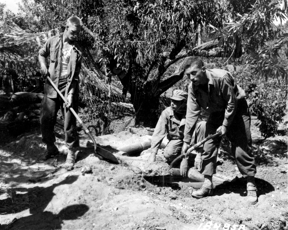 SC 184858 - L-R: Cpl. Elbert Pearson, So. Deerfield, Mass.; S/Sgt. Jack Boone, Montgomery, Ala., and Pvt. Charles Payne, Canton, Ohio, members of a Field Artillery unit near Niscemi, Sicily, cover their foxholes with empty shell boxes filled with dirt.
