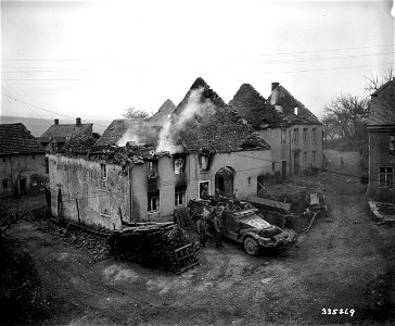 SC 335269 - A halftrack of the 10th Armored Division, U.S. Third Army, parks near smoldering building in newly captured Kall, Germany. 16 March, 1945.