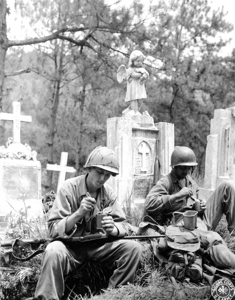 SC 396829 - Two members of the 129th Inf., 37th Div., eating C rations beside gravestones at Baguio Cemetary, Luzon, P.I.