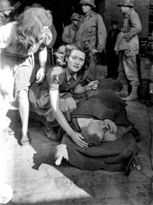 SC 195694 - Two German girls comfort their father who was seriously wounded by the explosion of an enemy delayed-action artillery shell that crashed into a factory basement where civilians had taken shelter in Bardenberg, Germany.