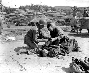 SC 349054 - HN(USN) Richard E. Rosegoom, Columbus, Ohio, and HM 1/C(USN) Frank J. Yasso, N.Y., med corpsmen assigned to the 1st Mar. Div., give first aid to a wounded North Korean near the river crossing. 20 September, 1950. photo