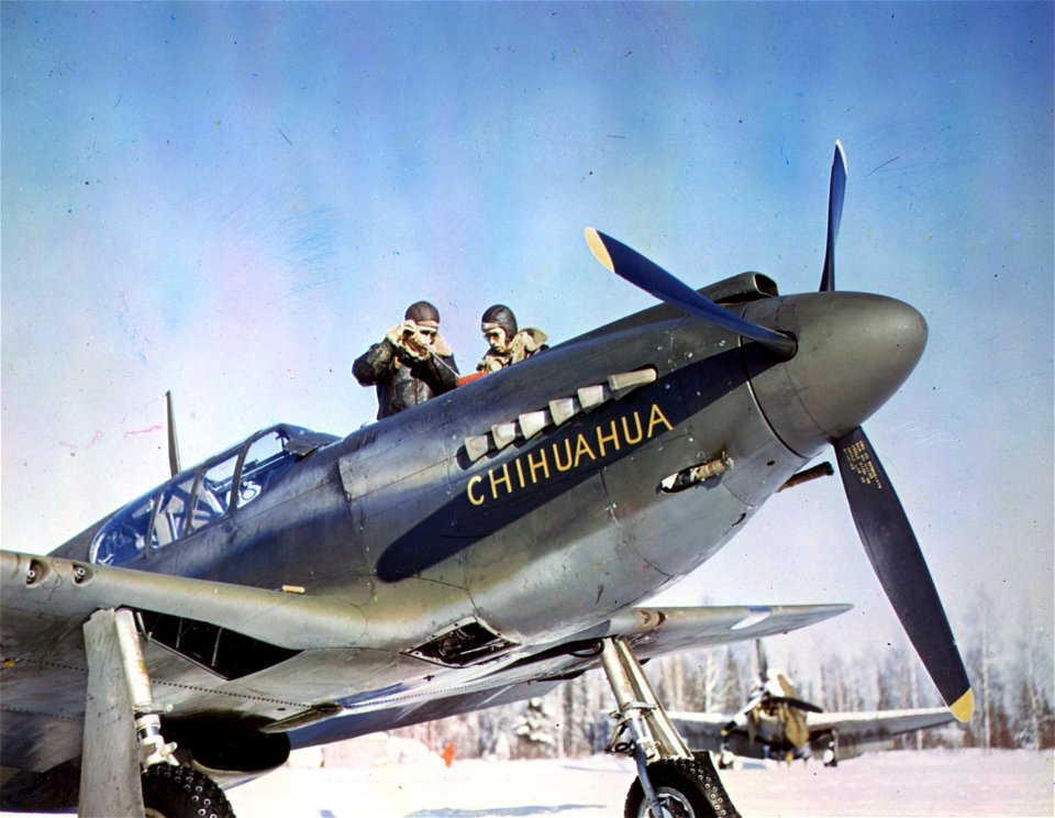 C-915 - Showing the front view of a P-51 with two pilots repairing the top of the plane. Alaska.