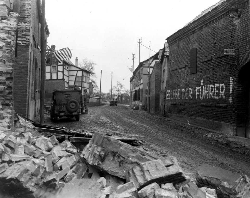 SC 336787 - A German patriotic slogan is painted on a wall in Schwerfen, Germany, while a white surrender flag flies from a building on the left right.