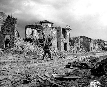 SC 329855 - In captured Cisterna, a U.S. soldier walks towards a dead German. Section of demolished Cisterna in background is typical of the rest of the town. 25 May, 1944.
