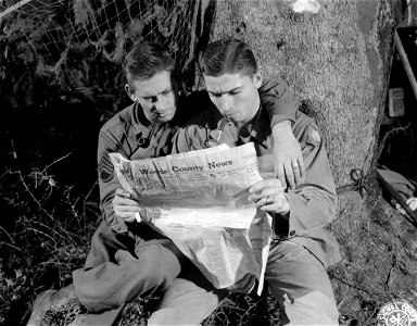 SC 396901 - S/Sgt. Leon D. Quinn and his brother, Cpl. Junior Quinn, both of the 45th Signal Company, read their hometown paper sent to them by their mother from Hopeton, Okla. photo