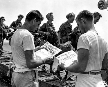 SC 396912 - Pfc. Ciro B. Iadavaio, Brooklyn, N.Y., and T/4 Ira W. Myer, Louisville, Kentucky, of the crew of the hospital ship "Marigold" getting their first printed news of the invasion on the southern coast of France...