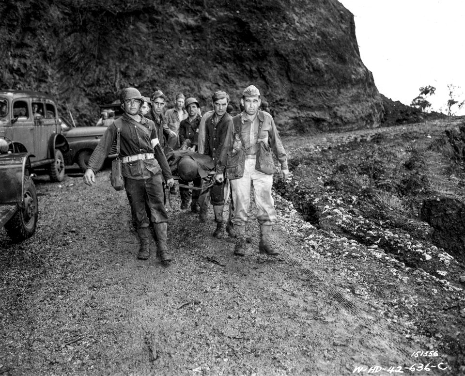 SC 151556 - Medical first aid units carry a soldier down the trail to a first aid station. It took eight men to carry one man over the rough trail during maneuvers.