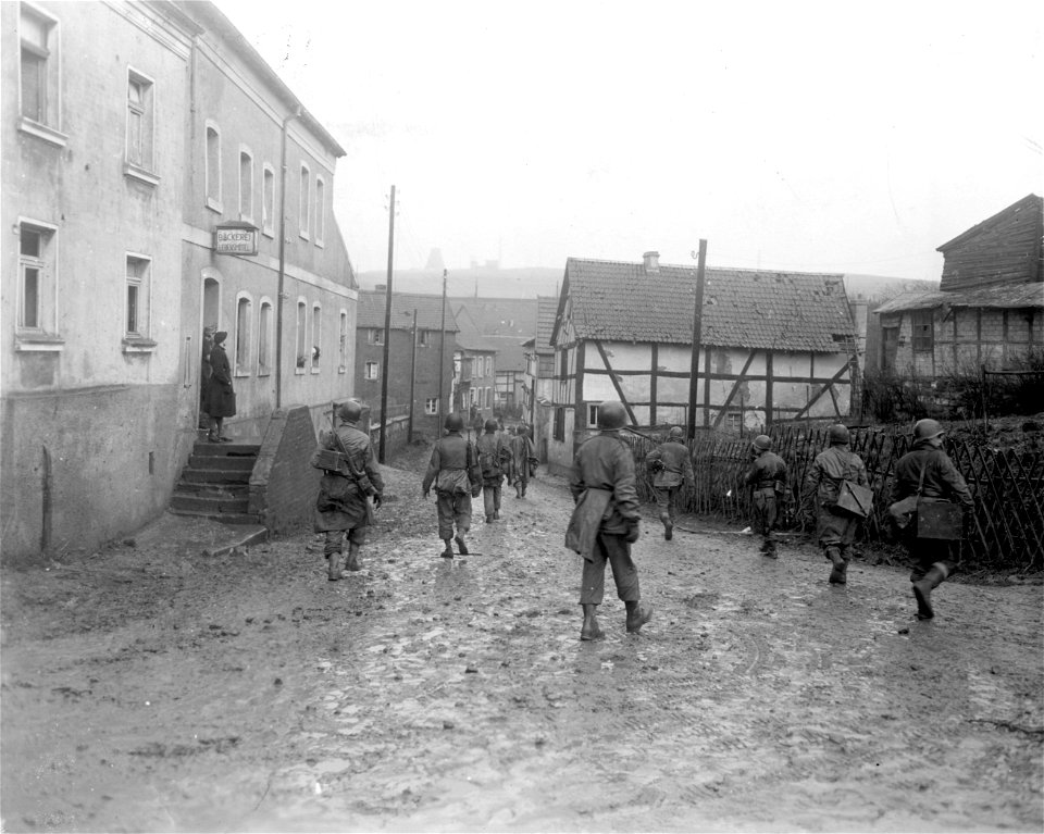 SC 270606 - Infantrymen of the 2nd Division, 1st U.S. Army, move through the streets of Scheven, Germany, Germany, as they advance towards Eiserfey, Germany. 6 March, 1945.