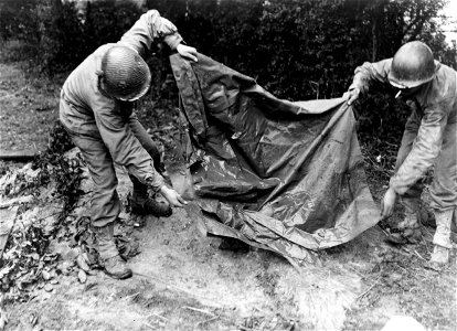 SC 396873 - Raincoat makes a roof for the foxhole shared by Pvt. T. M. Lauderdale, of Toccopola, Miss., and Pfc. William M. Sands, Stoneville, N.C. Here they pour rainwater from the coat during a storm in Holland.