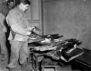 SC 364280 - S/Sgt. James Nolan, a member of the 134th Infantry Regiment, 35th Division, checks his German pistol in an army supply room before going on a pass into the city of Nancy. 6 December, 1944. photo