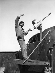 SC 364496 - Fireman 1st Class James I. Lynch, crew member of LCT, of Amelia, Virginia, stands by his .50 cal. machine gun on the bow watching for enemy planes, while subsistence supplies are being unloaded at Orange Beach, Arawe, New Britain.