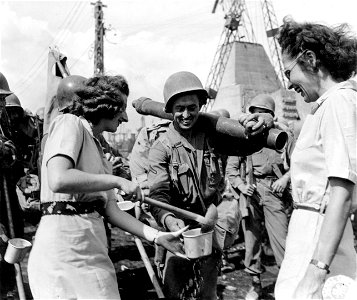 SC 329429 - Red Cross workers Nila Nevi, San Francisco, Calif., and Marge Busby, Claremont, Calif. ladeling out lemonade to Pvt. Fred Johnson, Russelville, Ala., who is among the soldiers loading for a future operation.