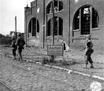 SC 195646 - Yank infantrymen pass a city limits sign of Aachen, Germany, still very much on the alert as Nazi snipers may be hidden in the building. 13 October, 1944. photo