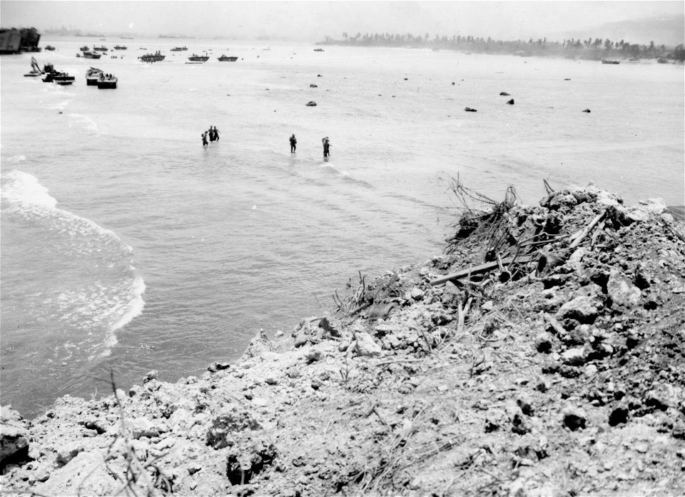 Marines come ashore, wading through surf as LSTs and smaller landing boats are hung up on coral, in left background. Saipan. June, 1944.