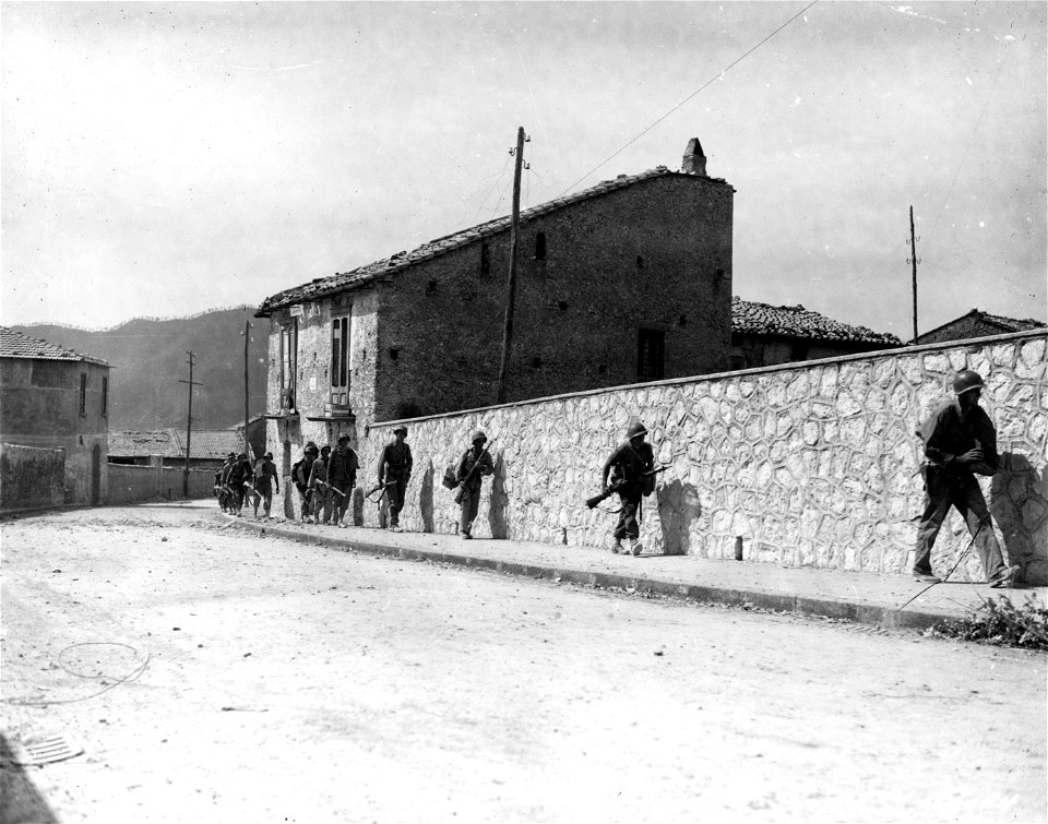 SC 180054 - Under intermittent enemy artillery fire, troops advance behind town wall. Acerno, Italy.