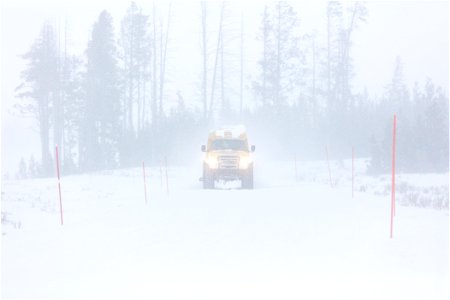 A snowcoach travels down the road during a winter storm