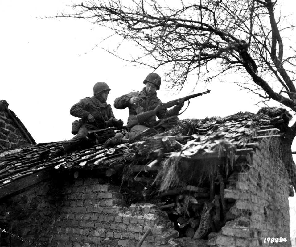 SC 198884 - S/Sgt. Urban Minicozzi, Jessup, Pa. (HQ Co.) and Pfc. Andy Masiero, Newburg, N.Y. (A Co.) stop to reload while sniping snipers from the roof of a building in Beffe, Belgium. 7 January, 1945.