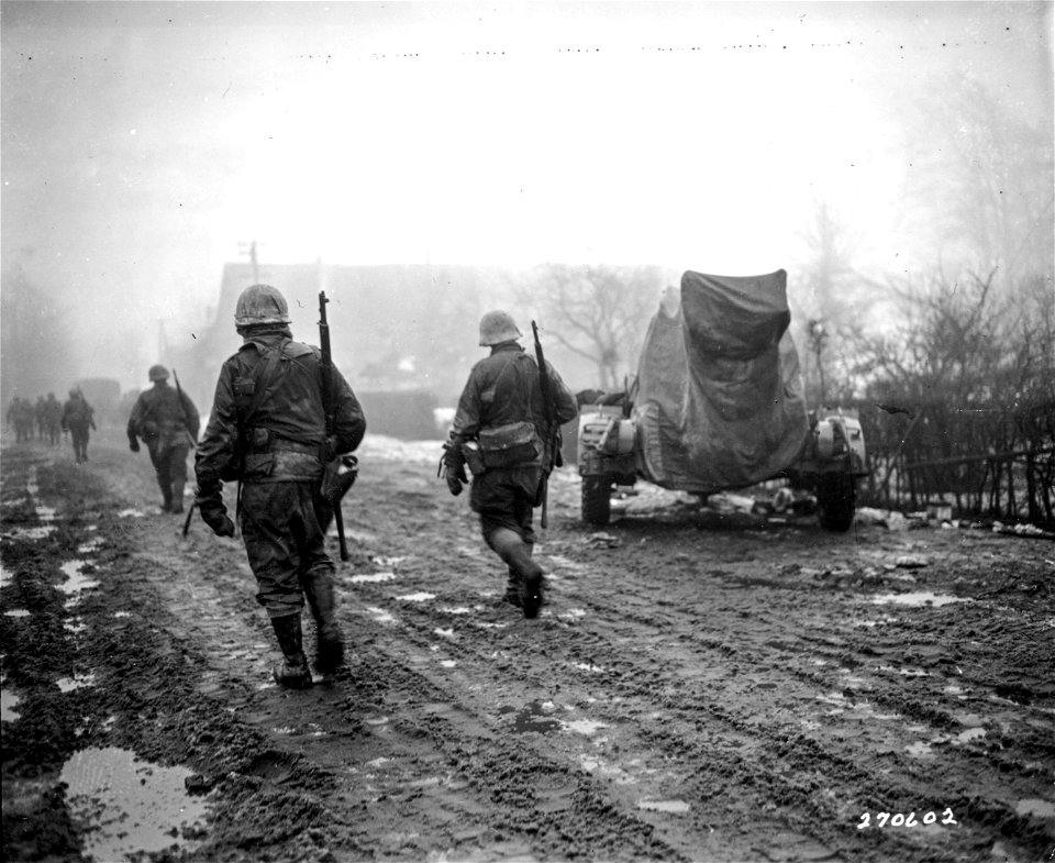SC 270602 - American infantrymen of the 2nd Infantry Division advance through fog into the town of Schoneseiffen, Germany, past an enemy antiaircraft gun abandoned when the Germans retreated. 3 February, 1945.