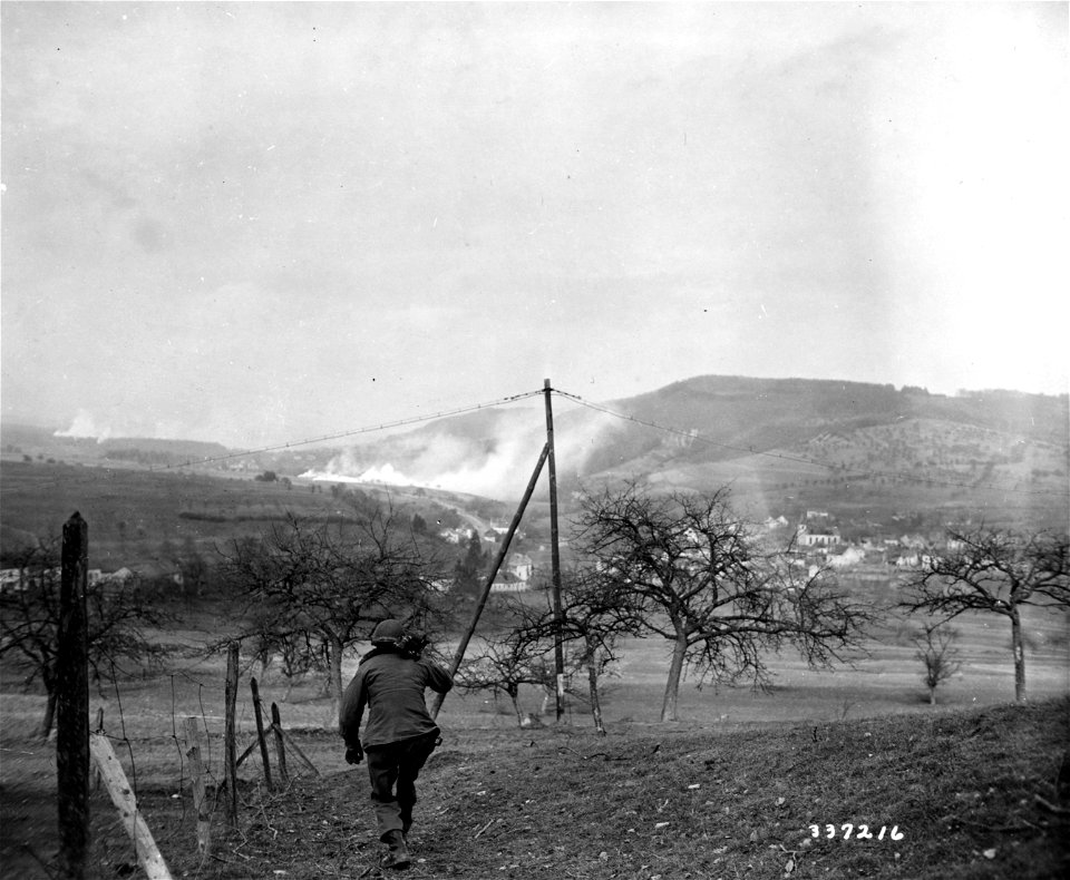 SC 337216 - Signal Corps cameraman S/Sgt. Raymond Graham, Los Angeles, Calif., carries his motion picture newsreel camera toward Holstheim, Germany.