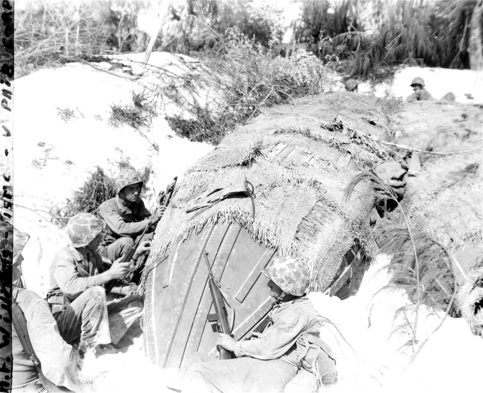 Marines squat behind Jap boat on beach. Saipan. June, 1944.
