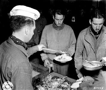 SC 195755-S - T/5 Miles J. Wermager, center, of Magnomen, Minn., a member of a cavalry unit near Monschau, Germany, receives his first piece of chicken since D-Day from T/4 Frank F. Leichtman, left, of Bresho, S.D. 31 October, 1944. photo