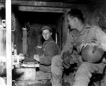 SC 195687 - Letter writing at the front: Sgt. Henry Gratzek, Orchard, Tex., at the typewriter and Pvt. Frank J. Allen, Rayeville, La., sit in an escape door of a Nazi pillbox. 17 October, 1944.