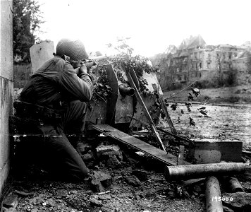 SC 195600 - Crouching in the shelter of a knocked-out German 47mm anti-tank gun in Aachen, Germany, Pvt. William Zukerbrow, Brooklyn, N.Y., draws a bead on a Nazi sniper. 19 October, 1944.