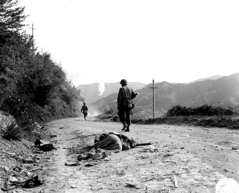 SC 195654 - Troops advancing into the Gothic Line area: dead German is in the foreground: phosphorous burst on hills in the background. 19 September, 1944.