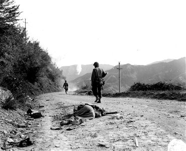 SC 195654 - Troops advancing into the Gothic Line area: dead German is in the foreground: phosphorous burst on hills in the background. 19 September, 1944.