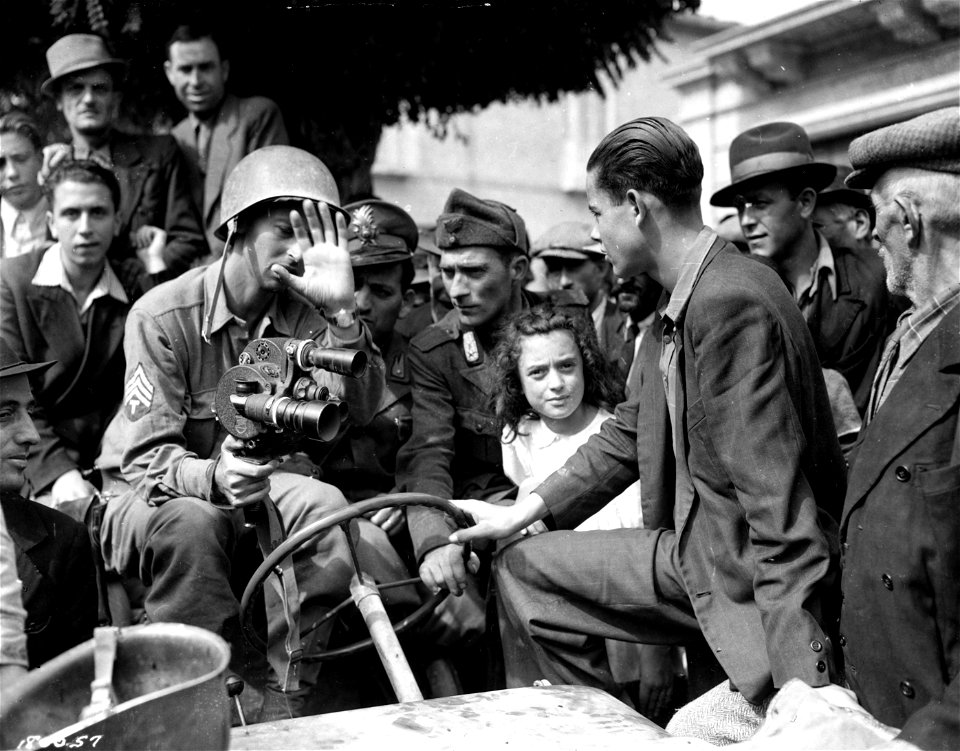 SC 180057 - T/4 David Kurland, Beverly Hills, Calif., APS, explains the workings of his "Eyemo" camera to local police and citizens, a few hours after Germans "vamoosed". St. Angelo, Italy. 28 September, 1943.