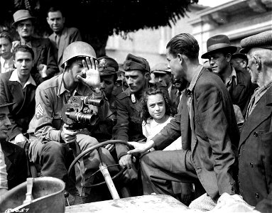 SC 180057 - T/4 David Kurland, Beverly Hills, Calif., APS, explains the workings of his "Eyemo" camera to local police and citizens, a few hours after Germans "vamoosed". St. Angelo, Italy. 28 September, 1943.