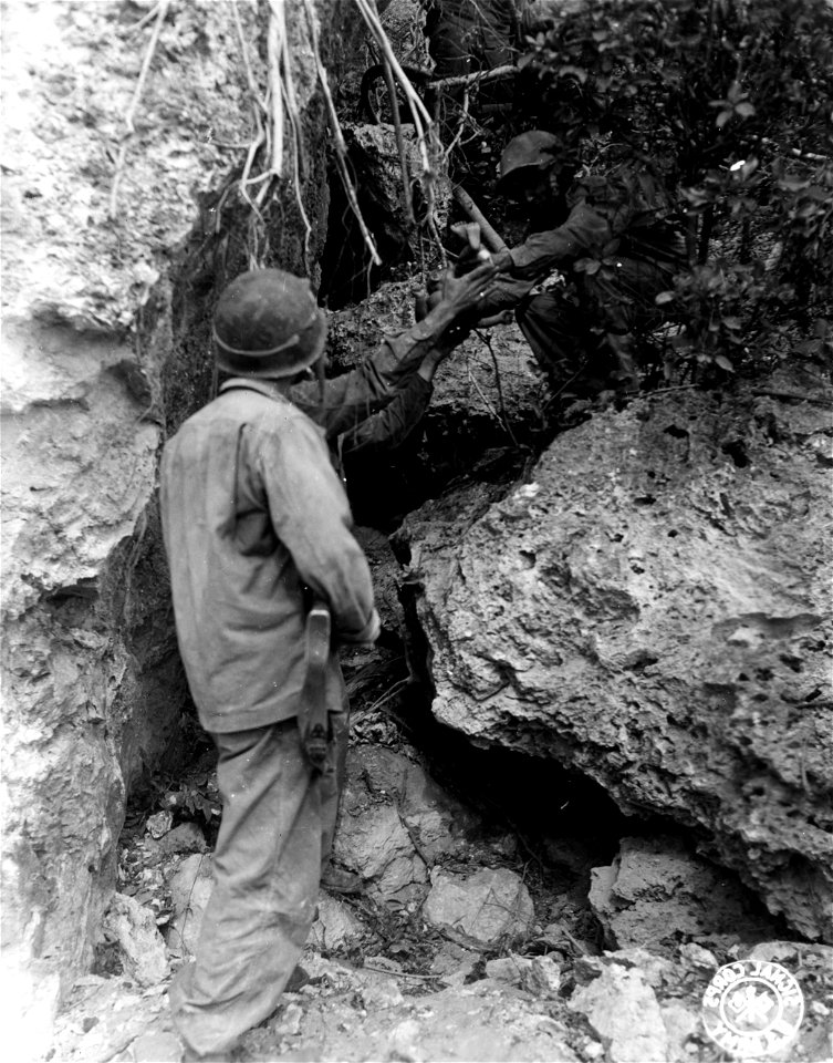 SC 405070 - American soldiers rescue Jap infant from small ledge partway up a steep rockpile along Nafuta ridge, bringing it down from its dangerous perch where it apparently was left by its parents.