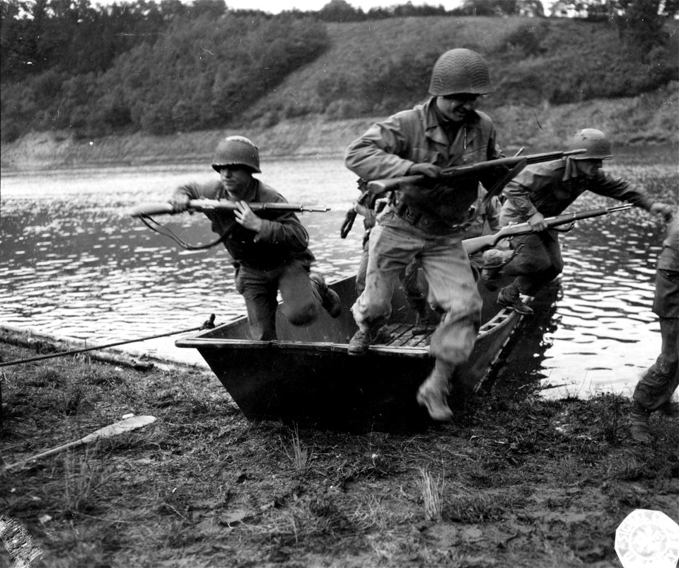 SC 195675 - Holding their rifles at high port, these GI infantrymen leap ashore as their storm boat makes a crash landing on the shore of a river somewhere in France.