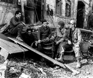 SC 334912 - W.P.G. Lt. James Scoggins sits outside the cellar of the battalion switchboard on a wire spool in the front line town of Rimling, France, talking over communications problems and other duties of combat infantrymen with Lt. Robert Altier... photo