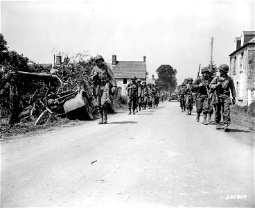 SC 270804 - American infantrymen march past a knocked-out 88mm gun and half-track used as a crew transport while on their way to the frontlines near Avranches, France. 31 July, 1944. photo